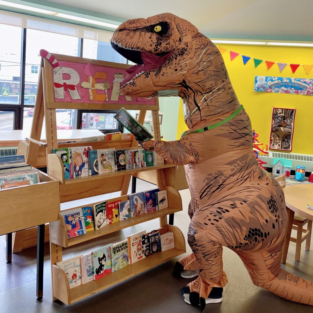 inflatable dinosaur looking at board books in children's library