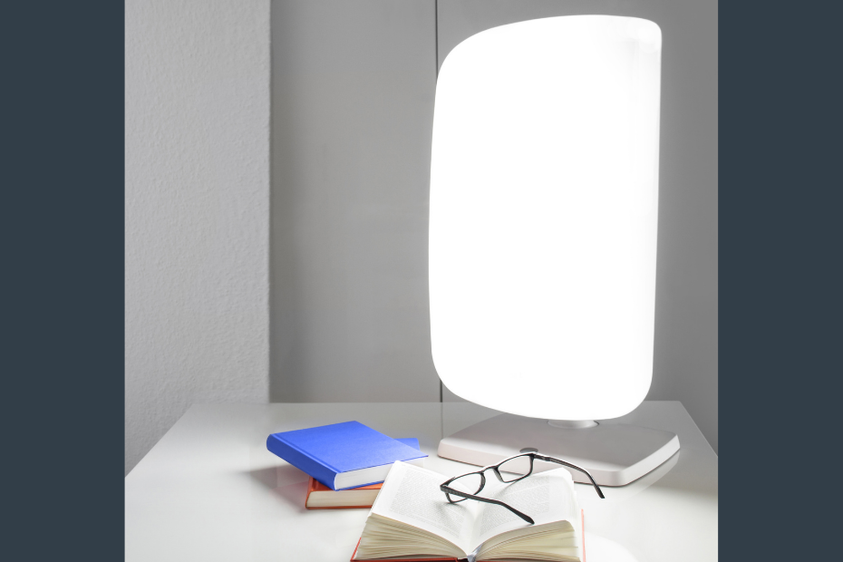 light therapy lamp on table with books and reading glasses