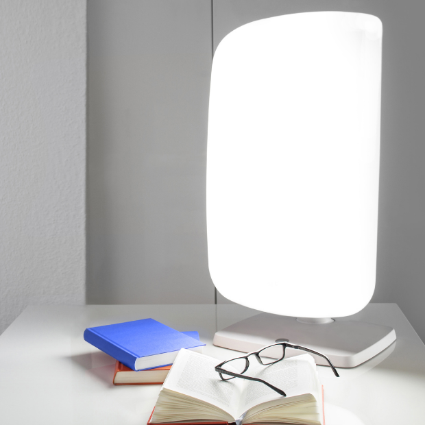 light therapy lamp on table with books and reading glasses