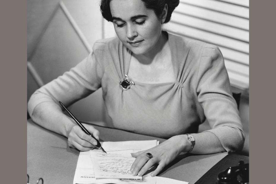 Black and white photo of woman sitting a desk writing letter circa 1950