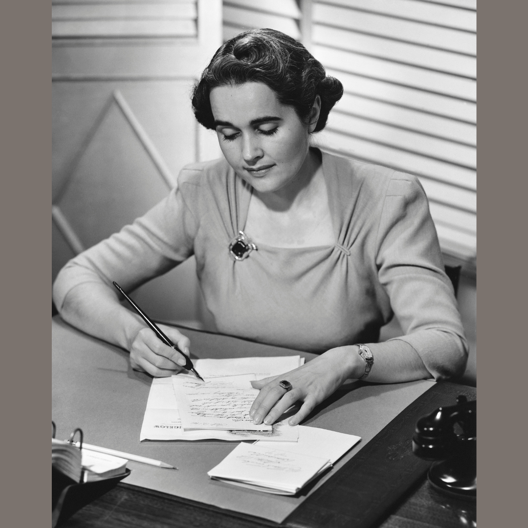 Black and white photo of woman sitting a desk writing letter circa 1950