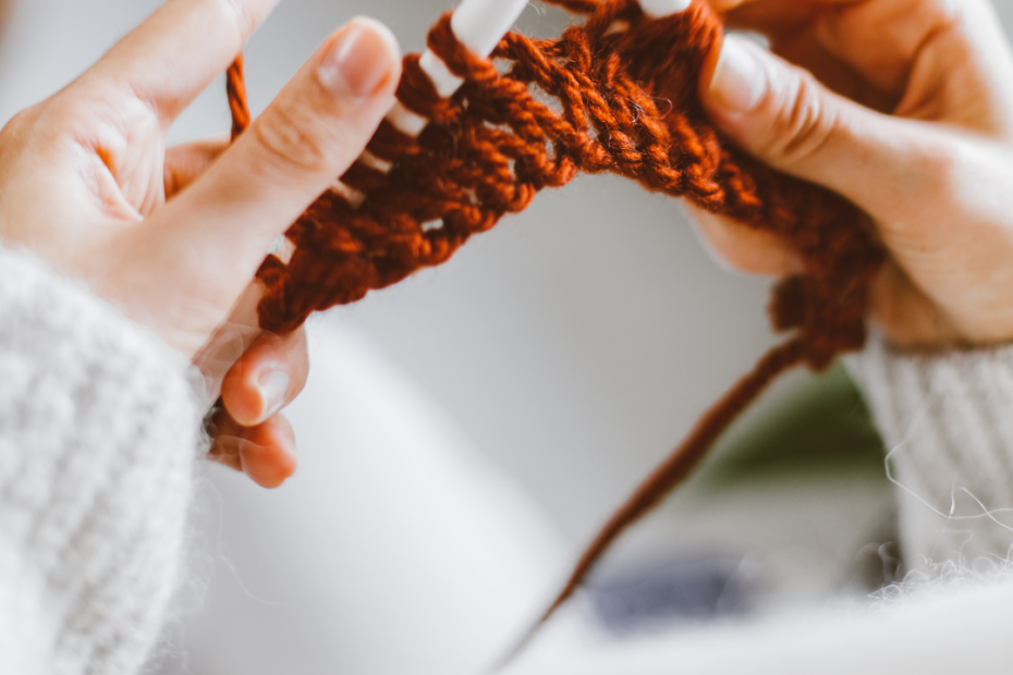 Photograph of two hands knitting from above.