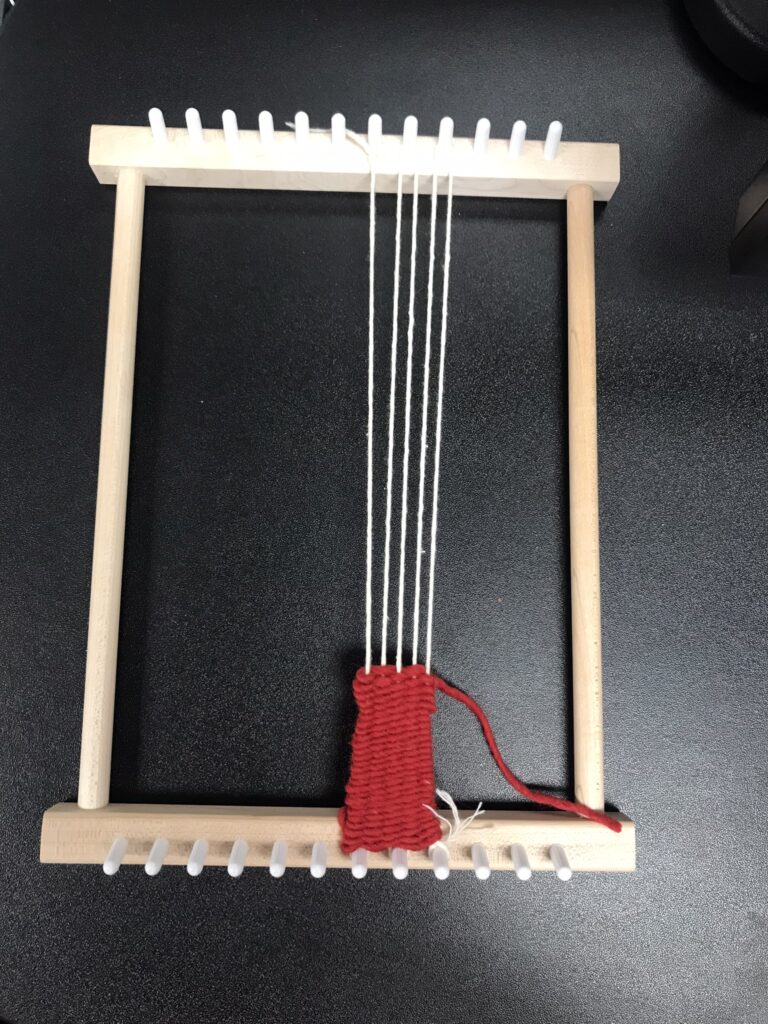 Peg Loom with warp string and weaving on centre three pegs only.