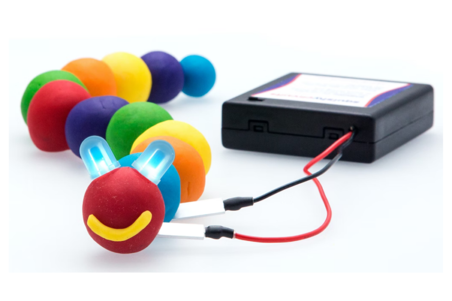 Squishy Circuit educational toy. Conductive play dough arranged to look like a caterpillar with LED light bulb eyes. Dough is connected to a battery terminal.